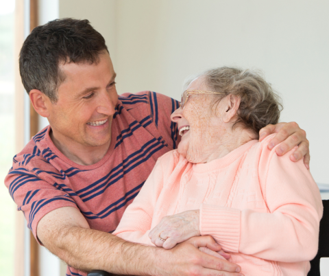 A younger man embracing an older woman while both are smiling 